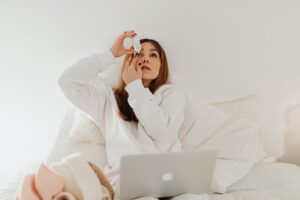 girl using eye drop with a laptop on her lap